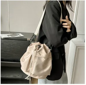 Detail van beige nylon emmertas met trekkoord en witte schouderband gedragen op lichaam
