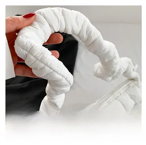 Close-up of white quilted puffer handbag featuring padded handle and top zipper detail