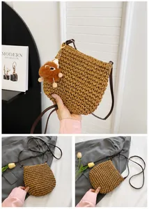 Detail van een bruine geweven stro schoudertas met een pluchen dierenhanger decoratie