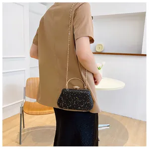 Detail of black evening clutch bag with golden glitter and sleek metal chain strap