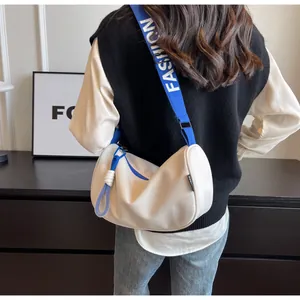Detail of white half-moon crossbody bag with blue fashion logo strap on female model