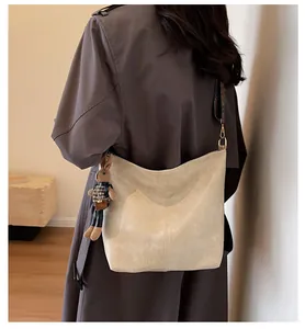Detail of cream tote bag with patterned strap and rabbit charm on a trench coat