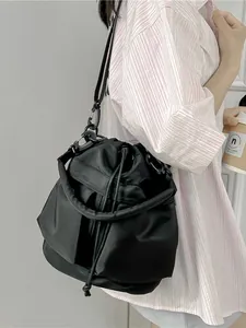 Zwarte nylon bucket bag met trekkoord en verstelbare riemen getoond in een lifestyle-model