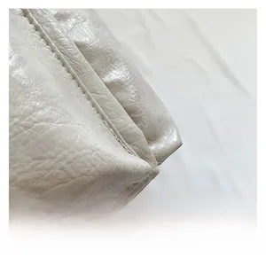 Close-up of creamy white glossy leather texture with fine stitching on a tote bag