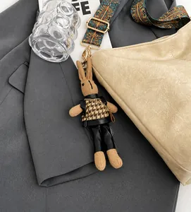 Detail of a brown knitted rabbit bag charm with houndstooth vest and gold chain