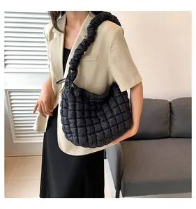 Detailopname van een zwarte gewatteerde puffer tas met geplooide schouderriem op model