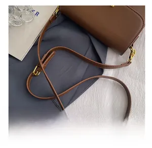 Detail of brown leather bag strap with adjustable gold buckle and metal hooks