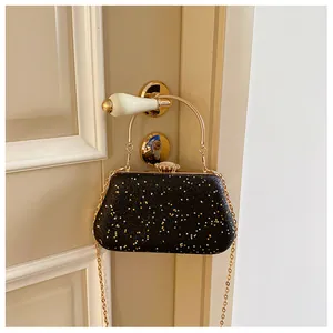 Close-up of black evening clutch bag with gold star sequins and metal arc handle