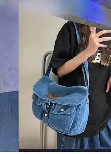 Close-up of blue washed denim messenger bag featuring front pockets and brown leather logo