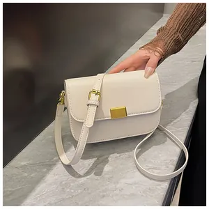 Close-up of cream leather crossbody bag featuring a golden rectangular buckle and marble background