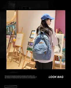 Detail des blauen Denim-Rucksacks mit Reißverschlusstasche und braunem Lederetikett