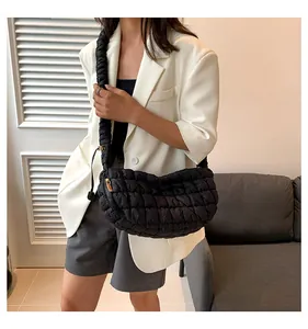 Detailed view of black quilted crescent shoulder bag with pleated strap on a model