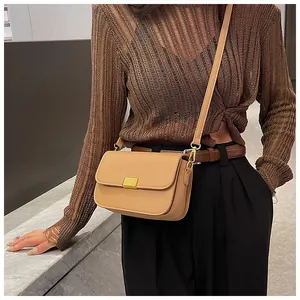 Detail of light brown leather crossbody bag with rectangle gold buckle on knitted top