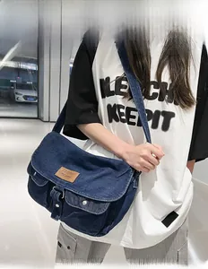 Detail view of denim messenger bag featuring double front utility pockets and logo