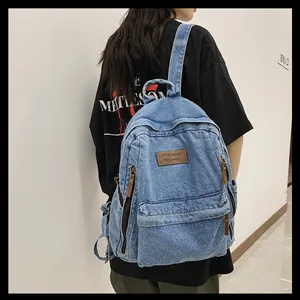 Side view of large light blue denim backpack with leather zipper pulls on a model