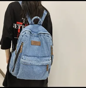 Close-up of washed blue denim backpack featuring leather logo patch and multiple zip pockets