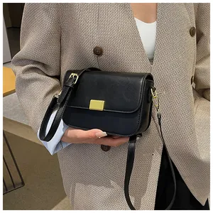 Detail of a black leather crossbody bag with a distinctive golden vertical striped metal buckle