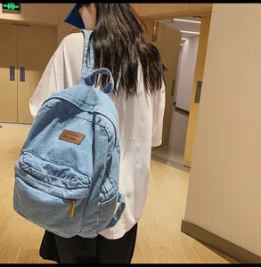 Detail eines hellblauen Denim-Rucksacks mit Reißverschlussfach und braunem Lederetikett