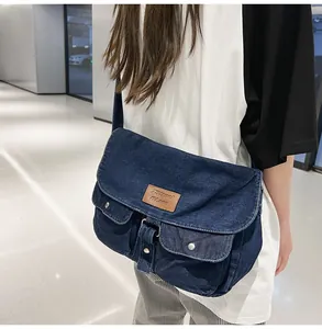 Detail of blue denim messenger bag featuring leather patch and silver metal buckles