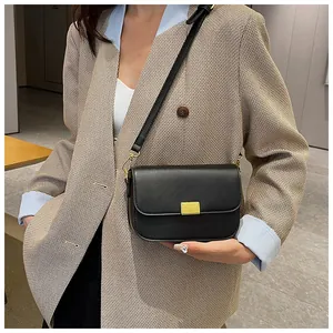 Close-up of a minimalist black leather crossbody bag with a gold rectangular metal clasp