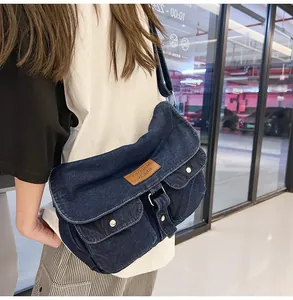 Detail view of denim crossbody bag showing two front pockets and brown leather brand patch