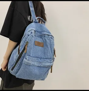 Detail of blue denim backpack with leather label and side zipper pocket on a model