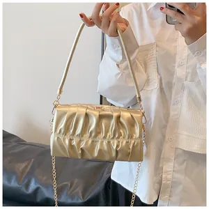 Detail der champagner-goldenen Faltenhandtasche mit starrem Griff und schlanker Metallkette