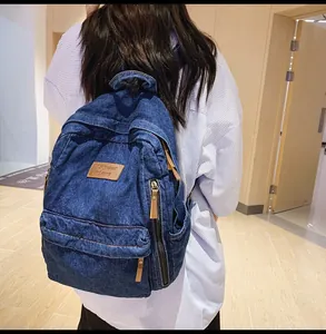 Detailed back view of a large blue denim backpack featuring washed texture and leather pulls