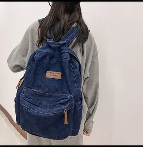 Detail eines dunkelblauen Denim-Rucksacks mit Leder-Logo und vorderer Reißverschlusstasche