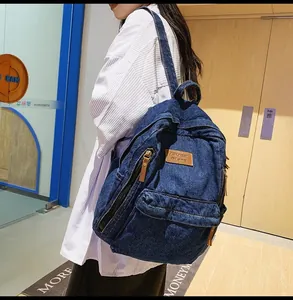 Detail of blue denim backpack showing multi-zipper compartments and leather logo patch