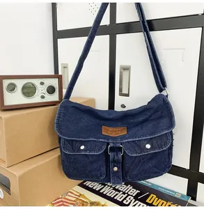 Detail of blue denim messenger bag with vintage utility pockets and leather logo patch