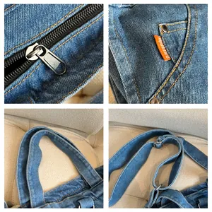 Detail view of denim tote bag showing sturdy zipper, orange brand tag, and adjustable strap