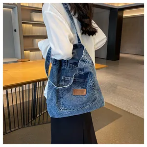 Detail of blue washed denim tote bag with leather patch and front pocket on shoulder