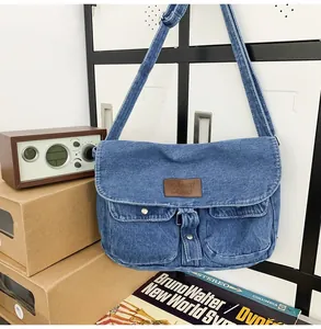 Detail of blue denim messenger bag featuring brown leather logo patch and two front pockets