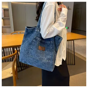 Macro detail of washed blue denim tote bag with leather logo tag and large outer pocket
