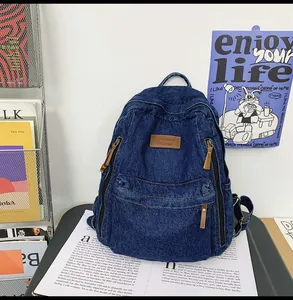 Detail of dark blue denim backpack featuring brown leather zipper pulls and logo patch
