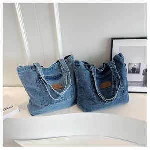 Detail of washed denim tote bag showing the front pocket and brown leather brand patch