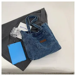Flat lay of washed denim tote bag with brown leather label on grey suit background