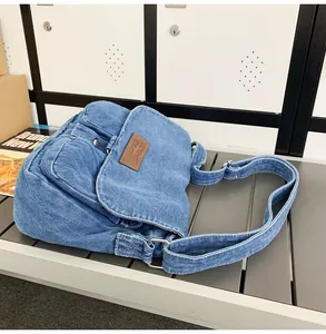 Detail of blue denim shoulder bag with brown leather logo patch and silver buckle strap