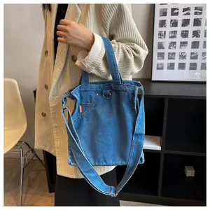 Detailed close-up of blue denim tote bag with orange label and adjustable shoulder strap