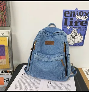Detail of blue denim backpack showing leather logo patch and brown zipper pullers