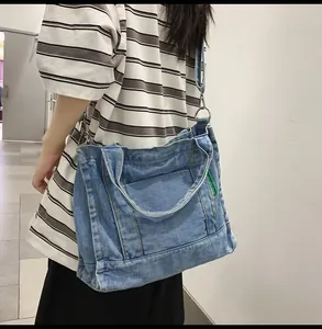 Detail of light blue denim tote bag with metal buckles and green brand label tag