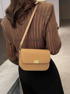 Minimalist khaki leather crossbody bag with a gold metal buckle worn by a model