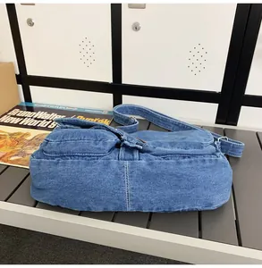 Detail of blue denim crossbody bag with white stitching and adjustable strap on a bench