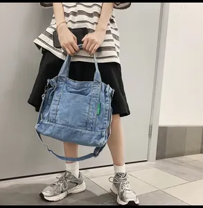 Detail of light blue denim tote bag with large front pocket and green woven brand tag
