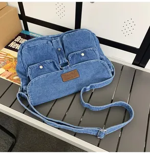 Detail view of washed blue denim crossbody bag with functional snap pockets and leather label
