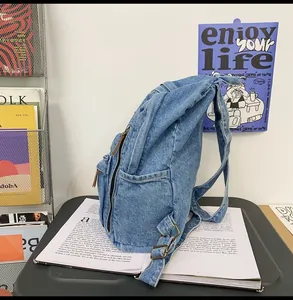 Detail of light blue denim backpack showing side zipper pocket and washed texture