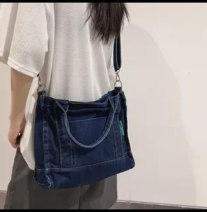 Detail of dark blue denim tote bag with side green label and metal strap hooks