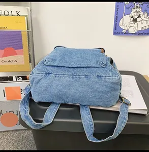 Detail of wide shoulder strap and reinforced bottom of a blue denim backpack