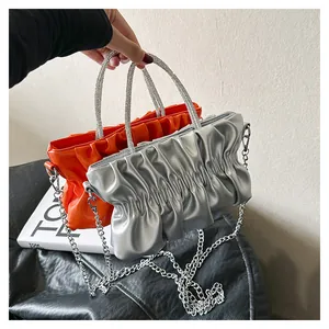 Detail of pleated cloud bags in orange and silver with rhinestone handles and chain